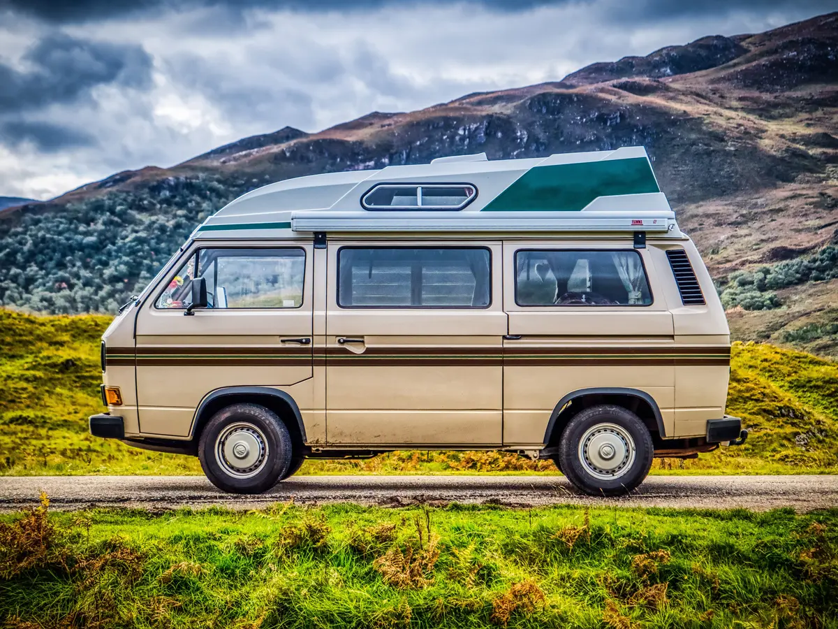 A Volkswagen T25 Transporter on a road in the green highlands of Scotland